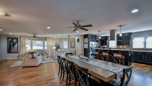 A spacious living area with a dining table, chairs, a sofa, and a kitchen area with dark cabinets and a tiled backsplash. - TuscaLodge: Close to Stadium, Big on Comfort! (Tuscaloosa)