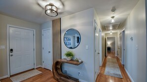 A hallway with wooden flooring, white walls, and a round mirror on the wall. - TuscaLodge: Close to Stadium, Big on Comfort! (Tuscaloosa)