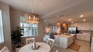 A modern kitchen with white cabinetry, a central island, pendant lighting, and a dining area with a round table and chairs.