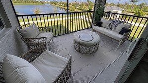 A balcony with wicker furniture, a round table, and a view of a lake and greenery.