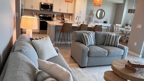 A modern living room with a grey sectional sofa, a round wooden coffee table, and a dining area with white furniture.