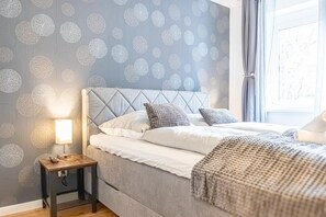 Ein Schlafzimmer mit einem Bett, Kissen, einem Nachttisch mit Lampe und einer Wand mit Muster.