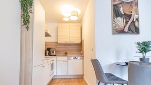 Una cucina compatta con mobili bianchi, lavastoviglie e zona pranzo con una sedia e un tavolo grigi.