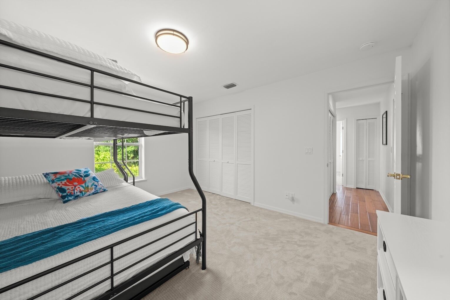 A bunk bed room with a window, white walls, and a door leading to another room.