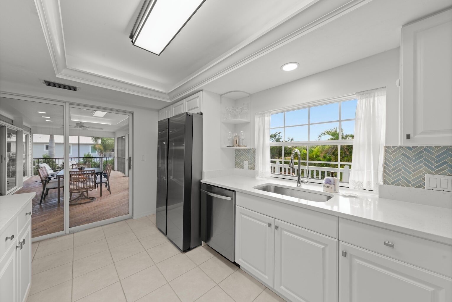 Una cocina moderna con armarios blancos, un refrigerador negro y una ventana con vistas a una terraza.