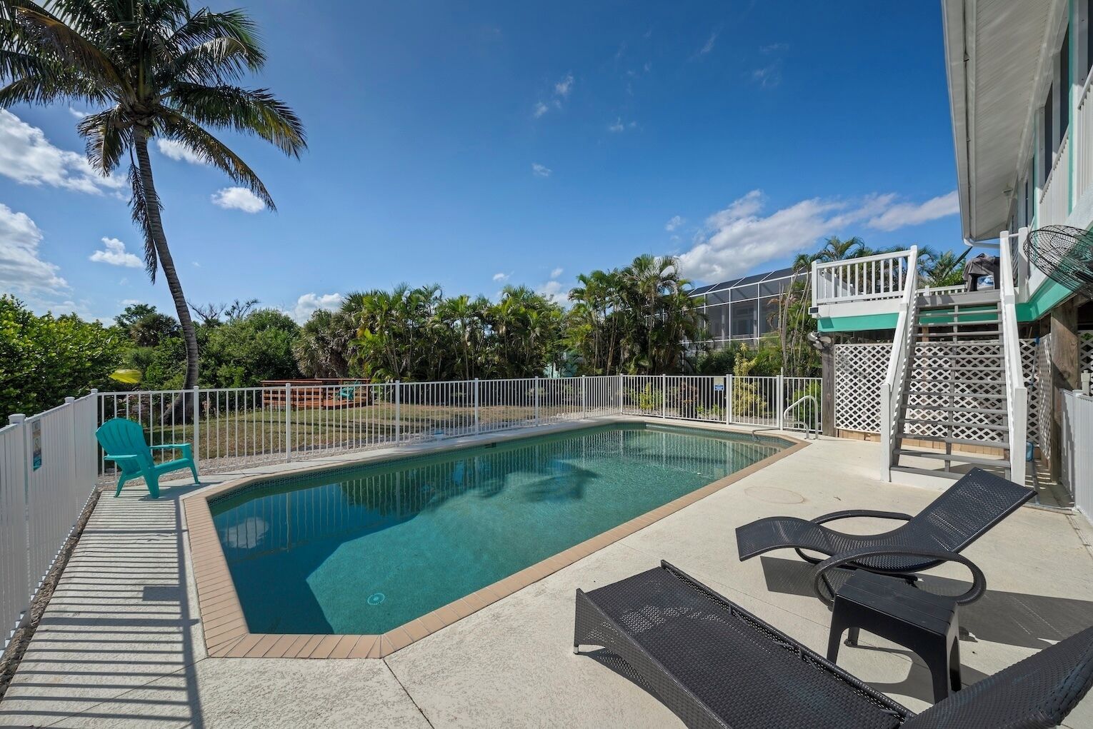 A rectangular pool with a white fence, lounge chairs, and a covered area with stairs.