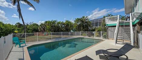 A rectangular pool with a white fence, lounge chairs, and a covered area with stairs.
