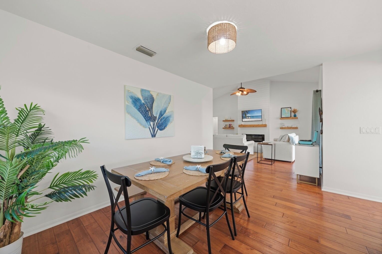 A modern living space with a wooden dining table, black chairs, a large potted plant, and a ceiling fan.