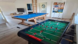 Ein Raum mit einer Fußballstoßmaschine, einem Billardtisch und einem Fernseher.