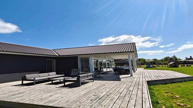 Ein modernes Haus mit überdachter Terrasse, einer Holzterrasse und einem Rasen.