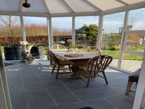 A conservatory with a dining table and chairs, large windows, and a view of the garden.