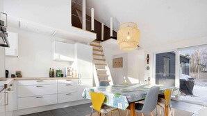 A modern kitchen with white cabinetry, a dining table with a colorful tablecloth, and a yellow chair. - 5 Star Holiday Home in Hals (Hals)