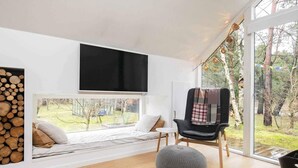 A modern living room with a large window, a mounted TV, a cozy seating area with a chair and ottoman, and a wooden floor. - 5 Star Holiday Home in Hals (Hals)