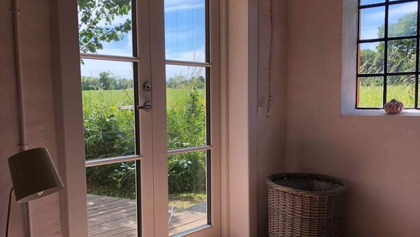 A room with a large sliding glass door leading to a wooden deck, a wicker basket, and a small table with a chair. - 5 Star Holiday Home in Svaneke (Svaneke)