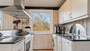 A modern kitchen with wooden cabinets, stainless steel appliances, and a window providing a view of trees. - 5 Star Holiday Home in Ronne (Ronne)
