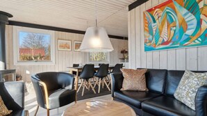 A modern living room with a black leather sofa, a round wooden coffee table, and black chairs. A large abstract painting adorns the wall, and a dining area is visible in the background. - 5 Star Holiday Home in Ronne (Ronne)