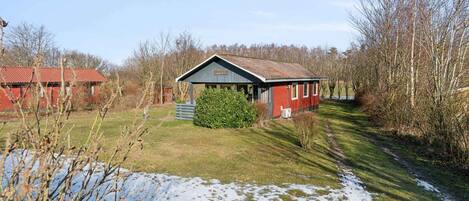 A red building with a sloped roof, surrounded by trees and a grassy area.