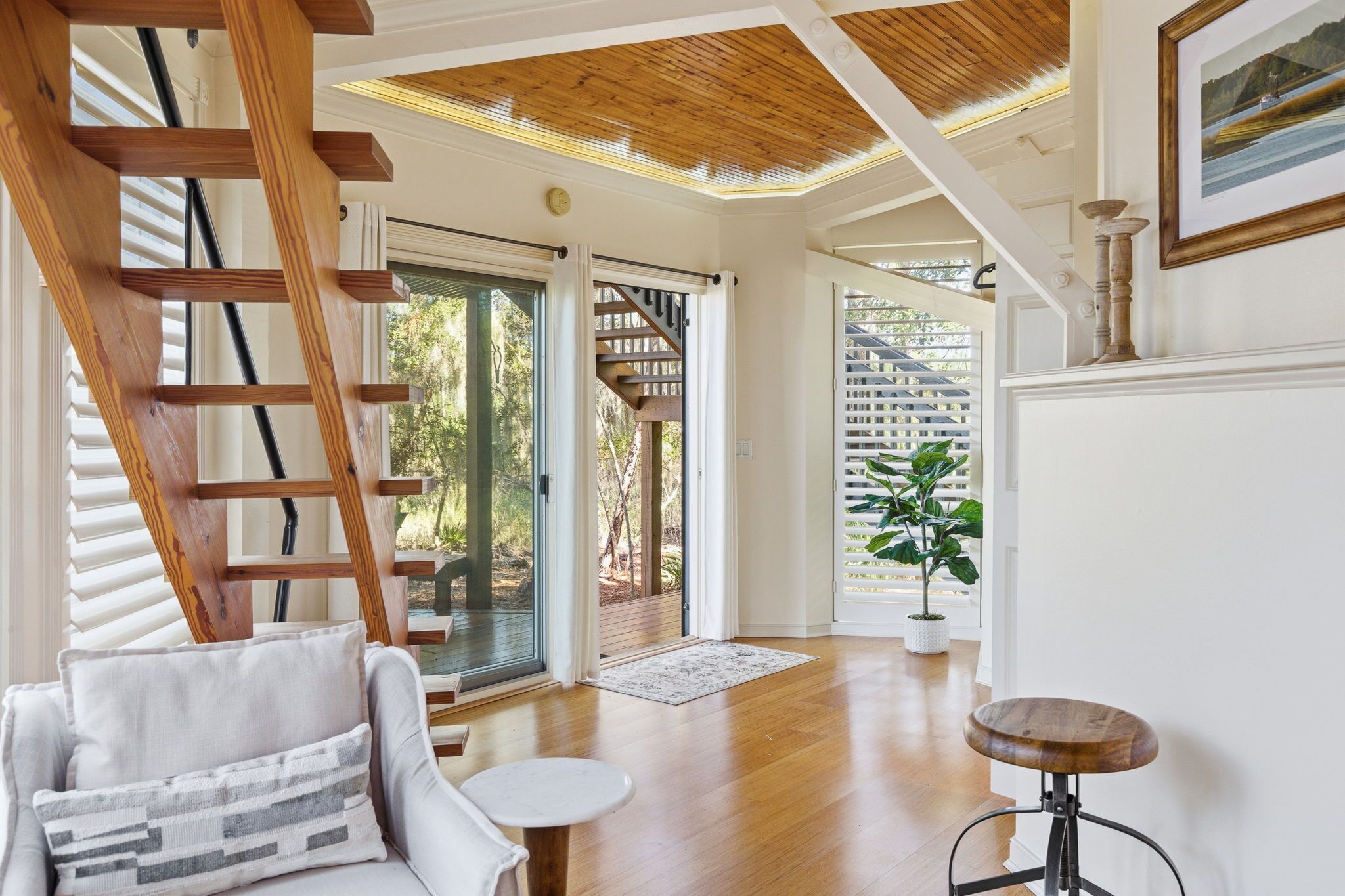 Une pièce spacieuse avec un escalier en bois, un fauteuil blanc, une petite table ronde et une plante en pot.