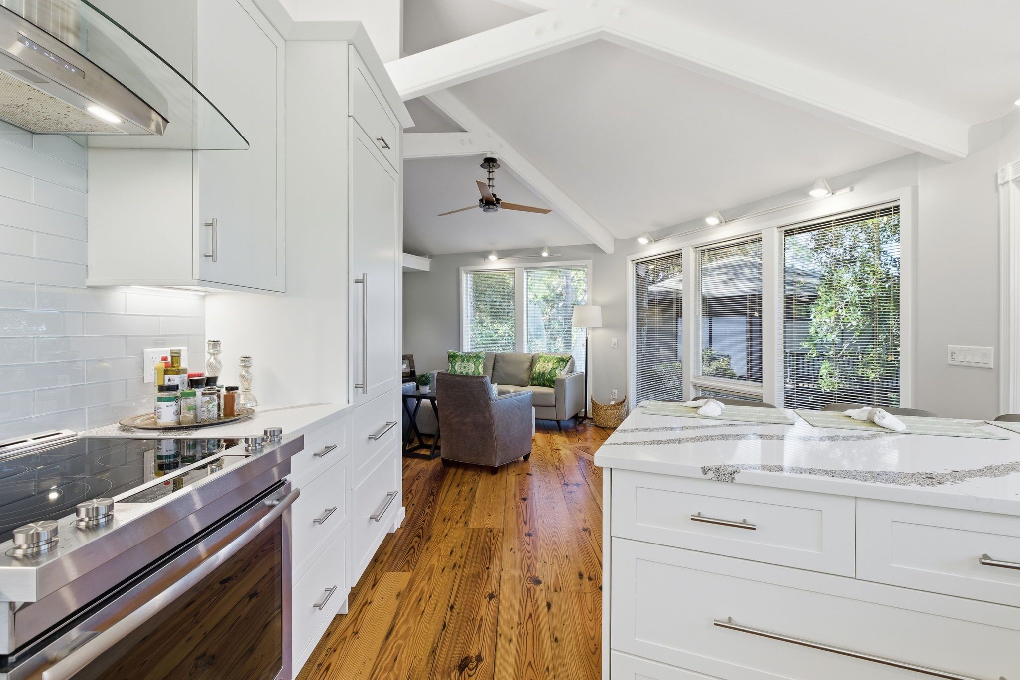 Une cuisine moderne avec des meubles blancs, un plancher en bois et un coin repas comprenant un canapé gris et un ventilateur de plafond.