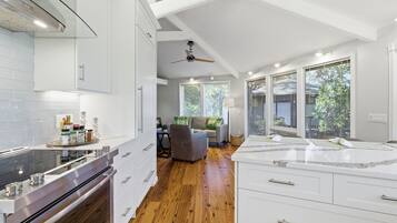 Une cuisine moderne avec des meubles blancs, un plancher en bois et un coin repas comprenant un canapé gris et un ventilateur de plafond.
