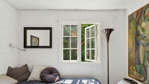 Ein Schlafzimmer mit einem Bett, Kissen, einem Fenster, einer Stehlampe und einem Gemälde.