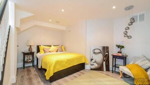 A modern bedroom with a bed, bedside table, lamp, and a chair with a throw blanket. - Elegant Ealing Apartment Retreat (Cape Town)