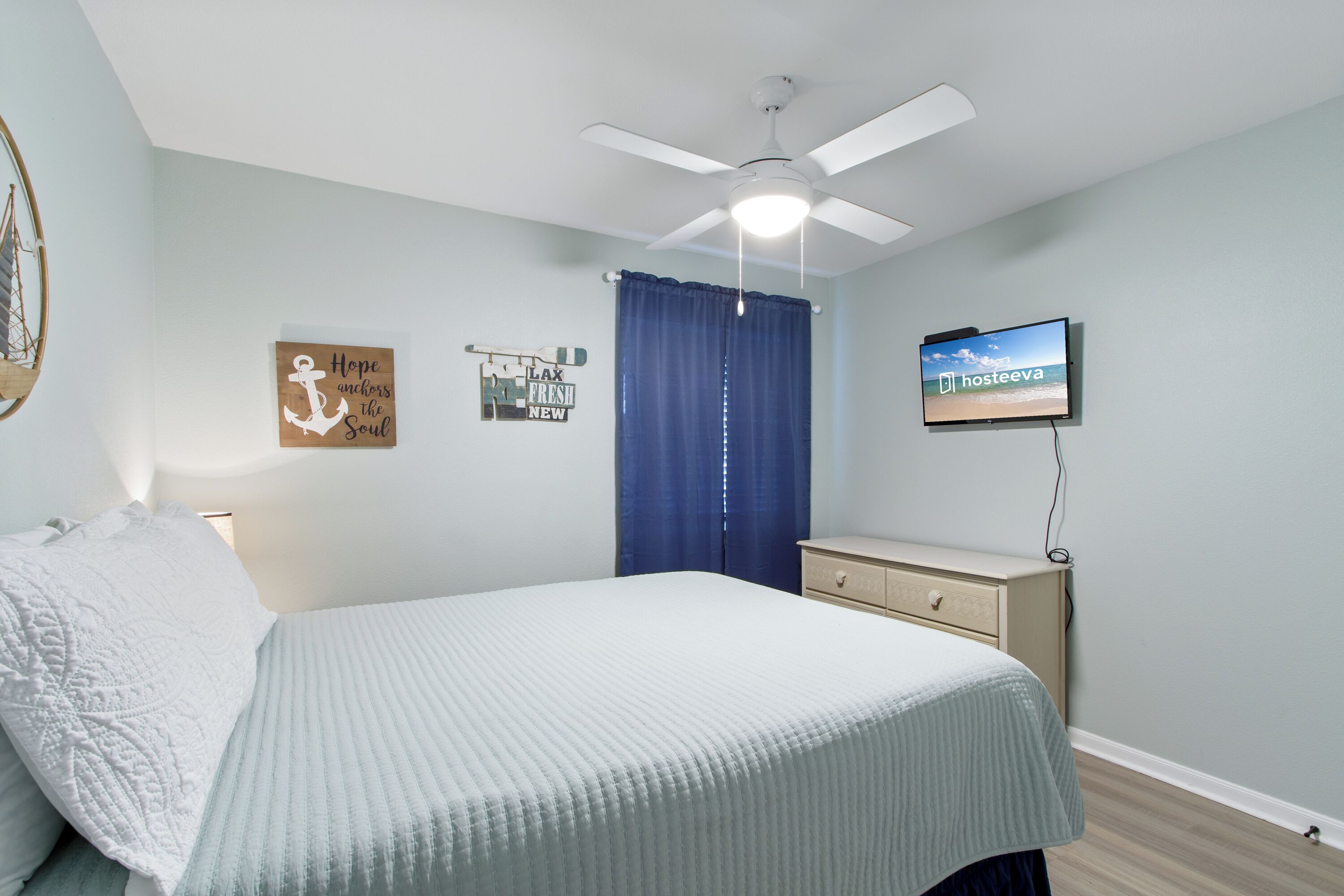 A bedroom with a bed, a ceiling fan, a TV, and wall art.