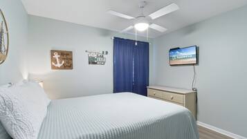 A bedroom with a bed, a ceiling fan, a TV, and wall art.