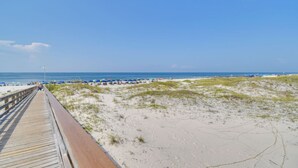 Ein Strand mit einer Holzpromenade, die zum Ufer führt, Sanddünen und Strandsonnenschirmen.