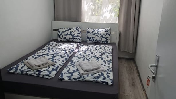 Una cama individual con una colcha estampada y almohadas, una ventana con cortinas y suelo de madera.
