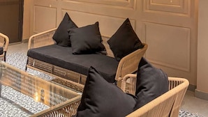 Un coin salon accueillant, avec des meubles et des coussins en osier, une table basse en verre et des luminaires fixés au mur.