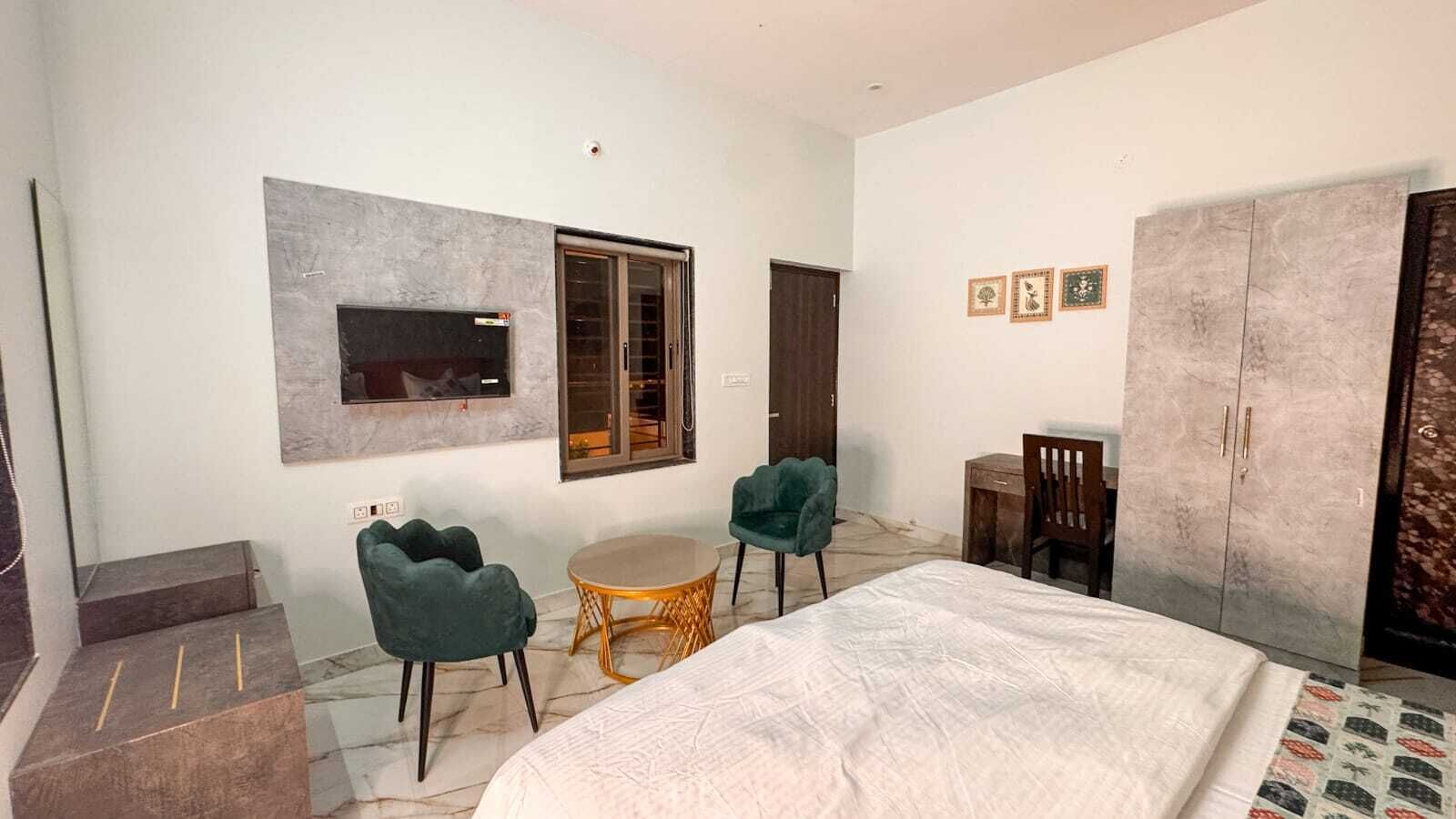 A bedroom with a bed, two chairs, a small table, a wardrobe, and a television mounted on the wall.