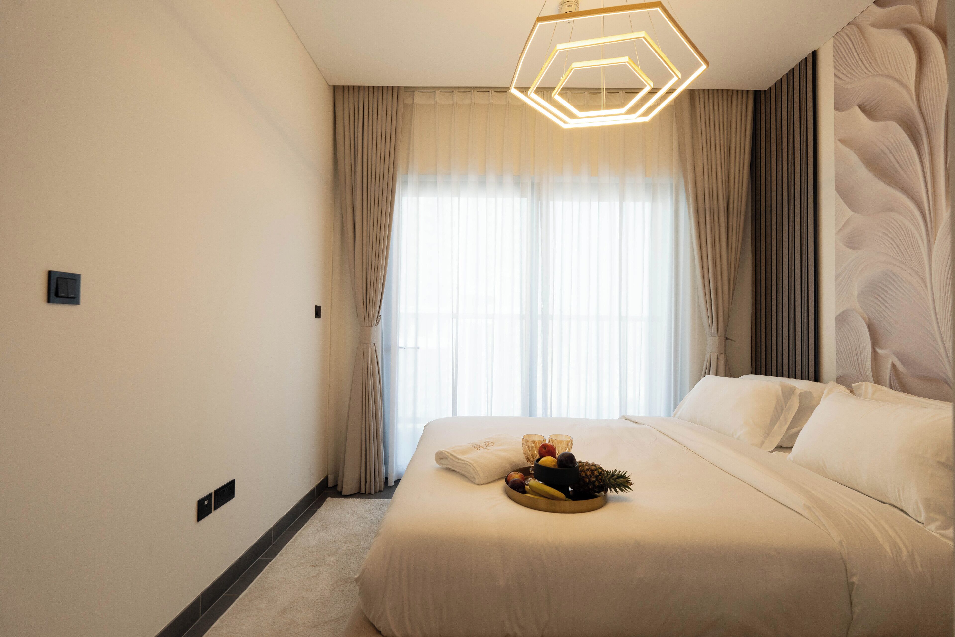 A hotel room with a large bed, a fruit and coffee tray, and a modern light fixture.