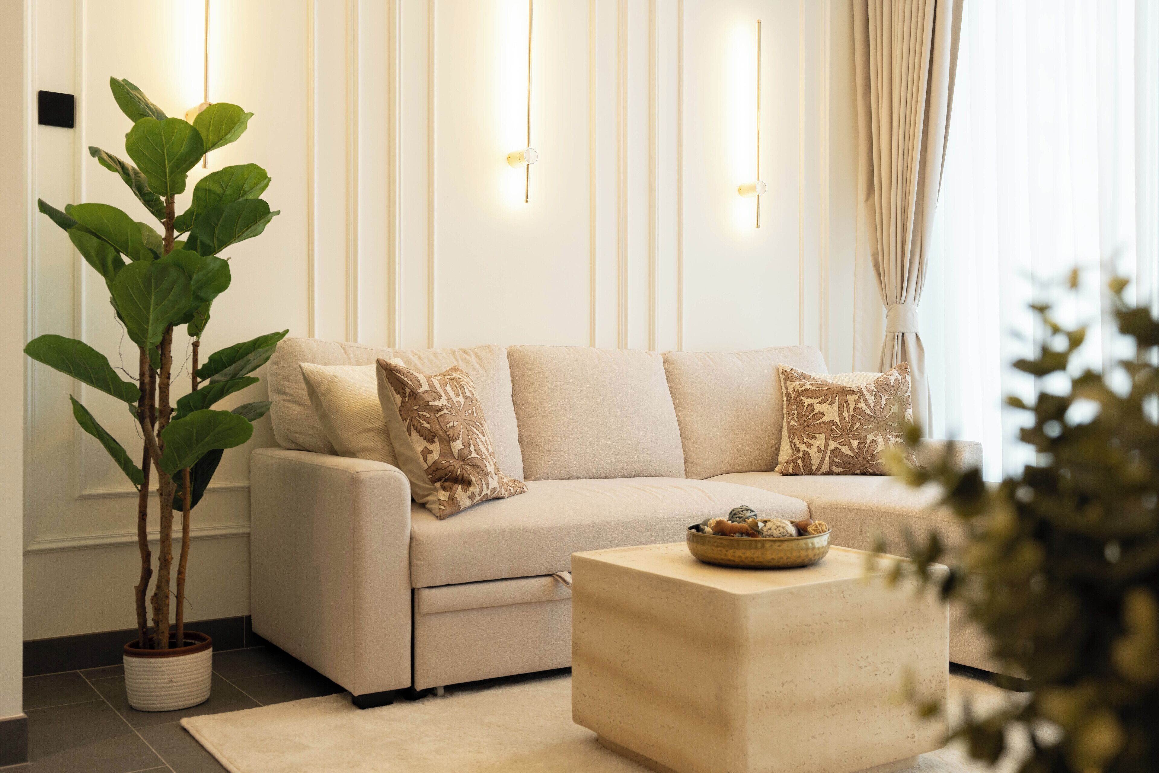 A modern living room with a beige sofa, decorative pillows, a potted plant, and a side table with a bowl.