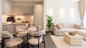 Uma cozinha moderna com armários brancos, um espaço de refeições com mesa e cadeiras redondas, e uma sala de estar com sofá e mesa de centro.