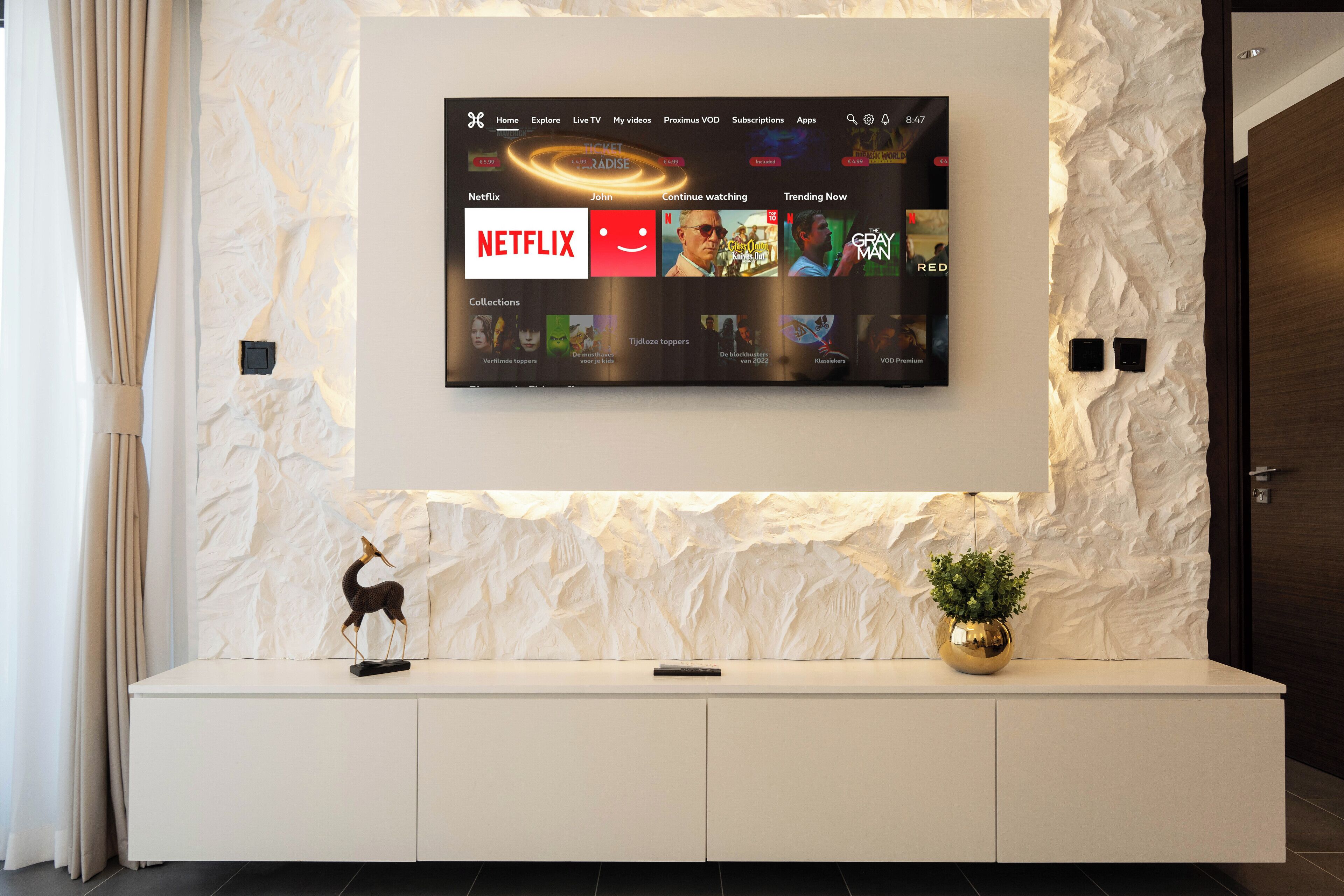 Een moderne woonkamer met een tv aan de muur waarop een streamingdienst draait.