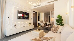 Uma sala de estar moderna com televisão de tela plana presa em uma parede texturizada, um sofá com almofadas estampadas e um espaço de jantar com cadeiras e uma mesa.