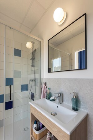 A modern bathroom with a glass shower enclosure, a large mirror, and a wooden vanity with a sink.