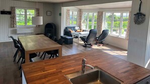 A modern kitchen with a wooden countertop, a sink, and a dining area with a table and chairs. There is a fireplace, a window with curtains, and a view of greenery outside. - 5 Star Holiday Home in Kirke Hyllinge (Kirke Hyllinge)