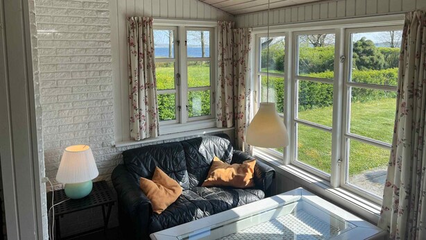 A cozy room with a black leather sofa, a glass coffee table, and a lamp. Large windows offer a view of a green landscape. - 5 Star Holiday Home in Kirke Hyllinge (Kirke Hyllinge)