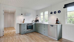A modern kitchen with white wooden paneling, a built-in oven, and a sink. There are two pendant lights, a window with a view, and a door leading to another room. - 5 Star Holiday Home in Kirke Hyllinge (Kirke Hyllinge)