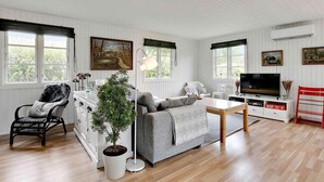 A cozy living room with a sofa, a coffee table, a TV, and a dining area with a table and chairs. There is a potted plant and a chair with a striped cushion. - 5 Star Holiday Home in Kirke Hyllinge (Kirke Hyllinge)