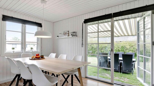 A dining area with a large table and white chairs, a hanging light fixture, and a view of the outdoors through large sliding glass doors. - 5 Star Holiday Home in Kirke Hyllinge (Kirke Hyllinge)