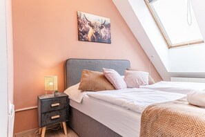 Een slaapkamer met een bed, nachtkastje, lamp en een schilderij aan de muur.