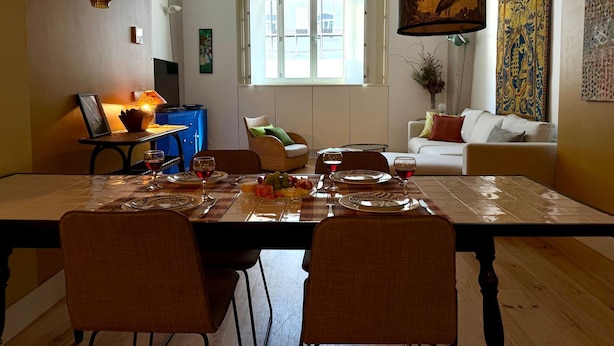 Un coin repas avec une table dressée pour quatre personnes, un buffet bleu, un canapé et une lampe suspendue.