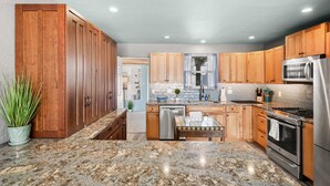 A modern kitchen with wooden cabinets, granite countertops, stainless steel appliances, and a small island with a sink. - Private Beach Access Sauna Outdoor Fireplace (St. Augustine)