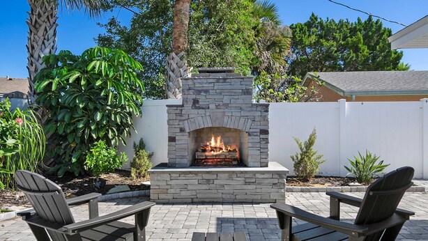 An outdoor patio with a stone fireplace, two Adirondack chairs, and a small table. - Private Beach Access Sauna Outdoor Fireplace (St. Augustine)