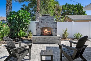 An outdoor patio with a stone fireplace, two Adirondack chairs, and a small table. - Private Beach Access Sauna Outdoor Fireplace (St. Augustine)