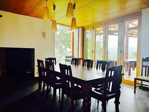 A dining area with a large table and chairs, a television, and large windows with a view.