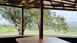 A spacious room with a large wooden table and a view of a green landscape through a wooden pergola. - Wandin Farm Views - architecturally designed home (Wandin North)